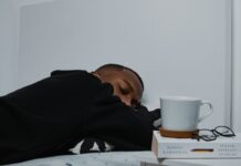수면 혁명, ‘마이크로 슬립’부터 AI 수면 관리까지…최신 트렌드로 건강하게 자는 법 a man sleeping on a bed next to a stack of books