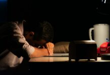 감정 억압이 위장과 흉부에 쌓이는 신체 감각의 정체 Man resting head on desk in dark room