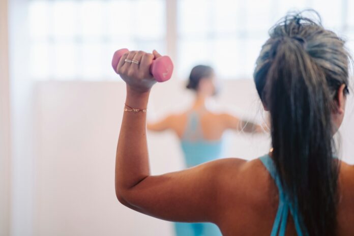 Photo by Alexandra Tran woman in blue tank top holding pink dumbbell